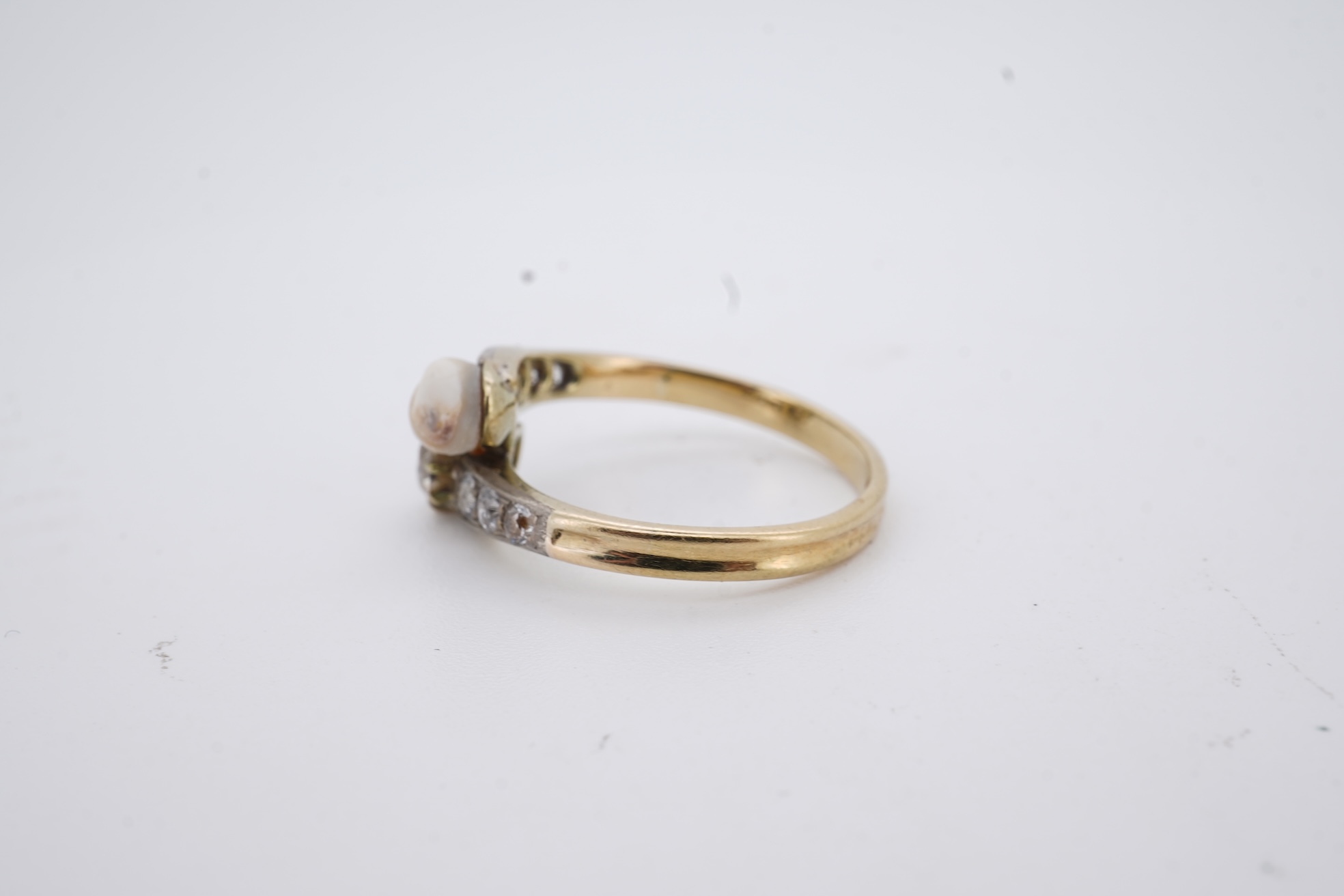 A yellow meta (stamped 18ct) cultured pearl and diamond set crossover ring, with six stone graduated diamond set shoulders, size M, gross weight 2.6 grams (pearl nacre a.f.).